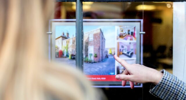 Jene femme devant une vitrine d'agence immobilière