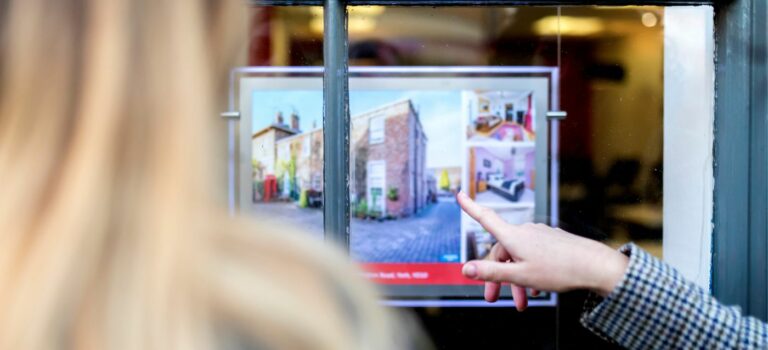 Jene femme devant une vitrine d'agence immobilière