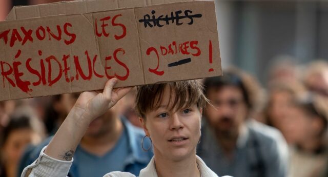 Jeune femme tenant dans les mains une pancarte : Taxons les résidences secondaires en Bretagne