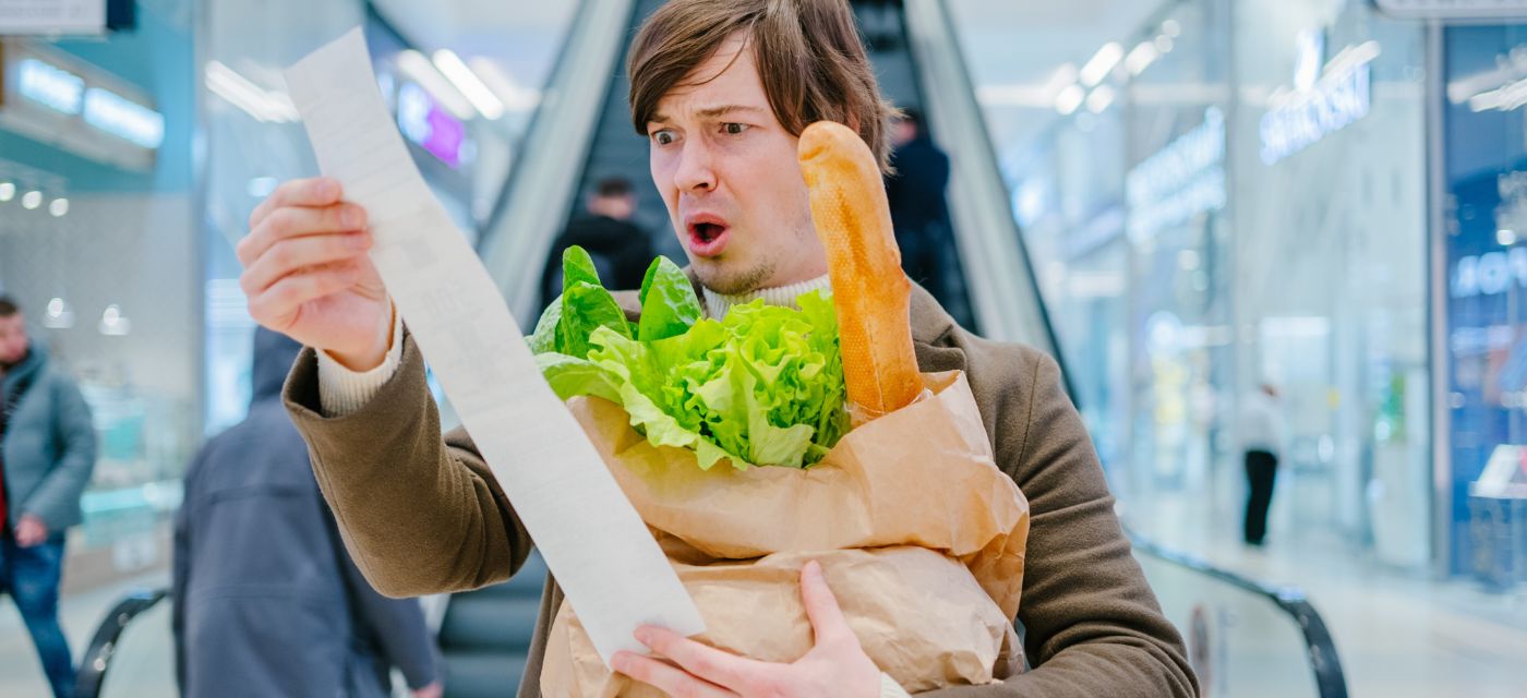 homme en train de regarder son ticket de caisse avec ses courses dans les bras