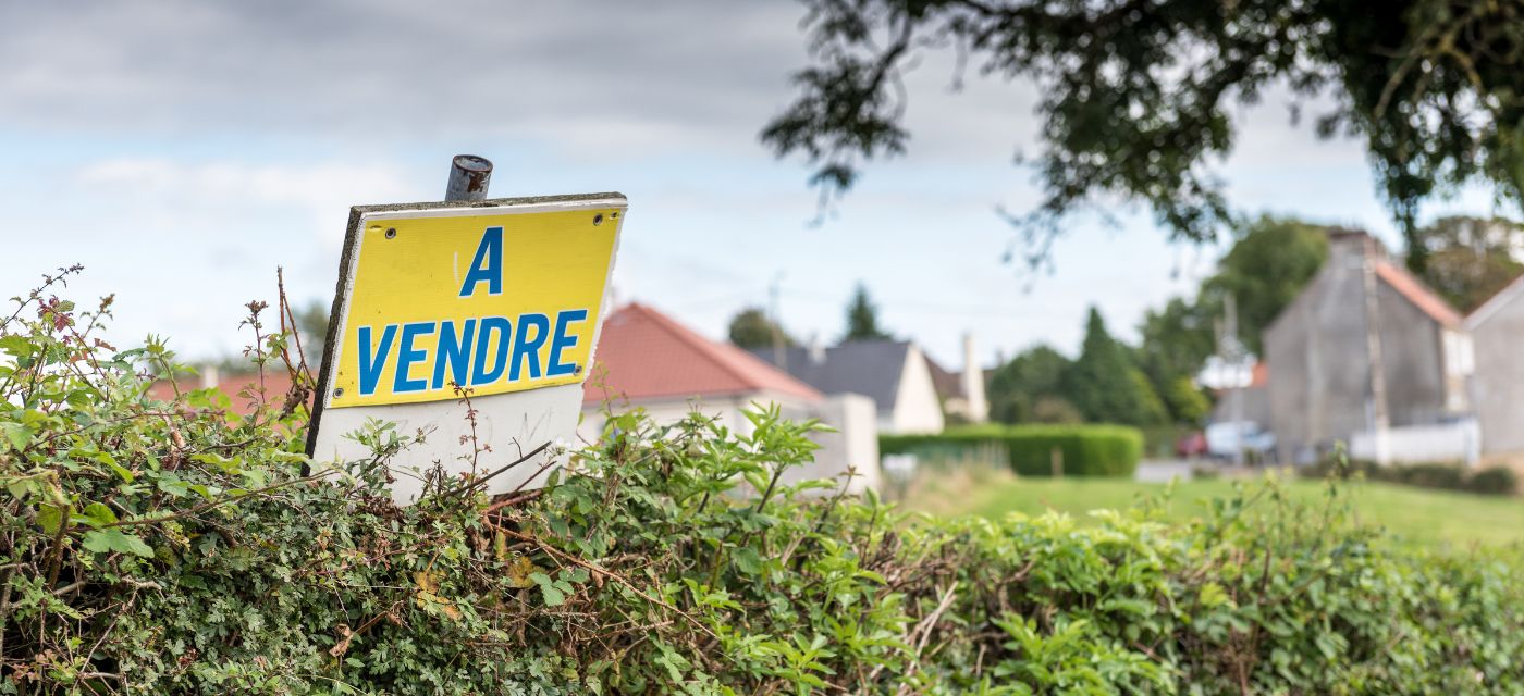 Pancarte à vendre posée sur un terrain devant une maison