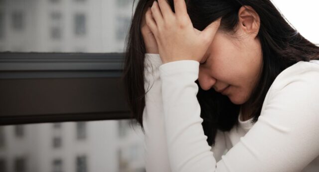 Jeune femme se prenant la tête devant une fenêtre