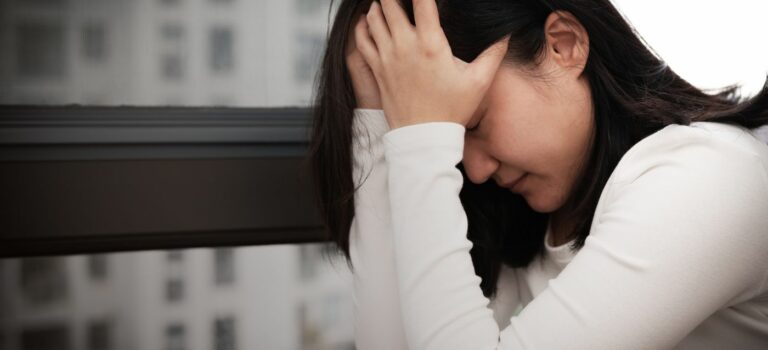 Jeune femme se prenant la tête devant une fenêtre