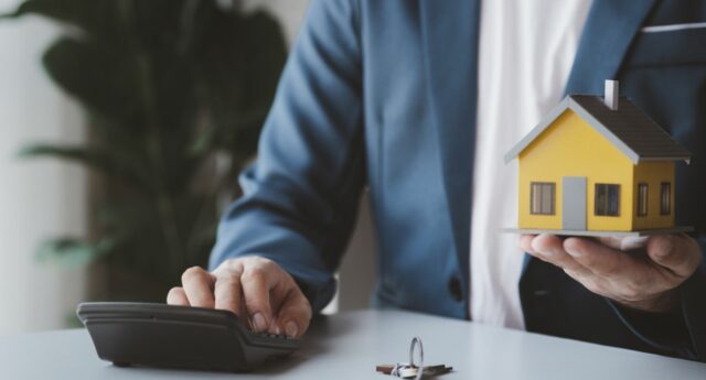 homme avec une calculatrice dans une main, et une maison miniature dans l'autre