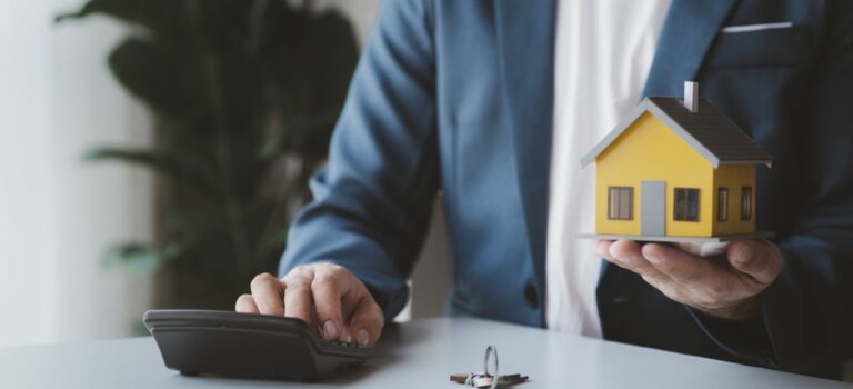 homme avec une calculatrice dans une main, et une maison miniature dans l'autre