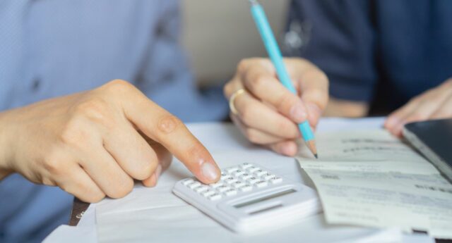 Couple ayant des difficultés financière en train de faire des calculs avec une calculatrice et un crayon à papier.