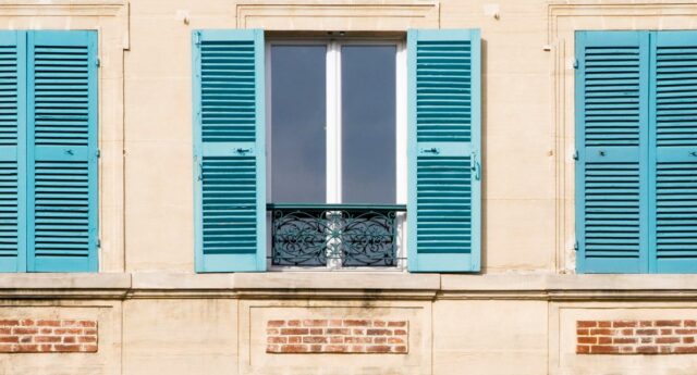 facade d'immeuble ancien avec trois fenetres et des volets verts ouverts et fermeés