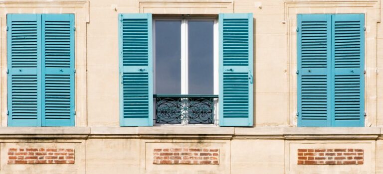 facade d'immeuble ancien avec trois fenetres et des volets verts ouverts et fermeés