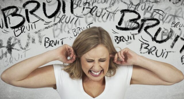 Femme souffrant de nuisances sonores et se bouchant les oreilles devant un mur avec graffitis bruits