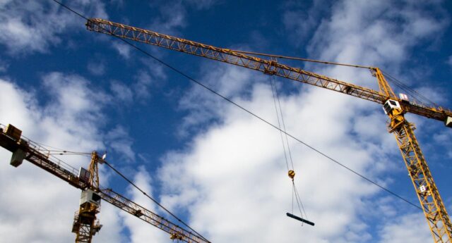 Des grues sur un chantier sur un fond de ciel nuageux pour illustrer la baisse des permis de construire