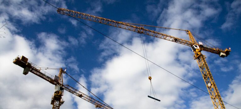 Des grues sur un chantier sur un fond de ciel nuageux pour illustrer la baisse des permis de construire