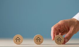 Une main attrapant un jeton en bois avec une maison dessinee dessus pour illustrer l'investissement immobilier en SCPI