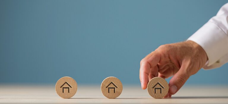 Une main attrapant un jeton en bois avec une maison dessinee dessus pour illustrer l'investissement immobilier en SCPI