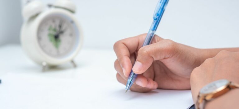 Femme tenant un stylo dans sa main et signant un document avec reveil en arriere plan pour illustrer le droit de retractation en immobilier