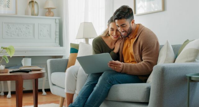 Couple sur un canapé en train de rechercher un bien immobilier sur un ordinateur portable