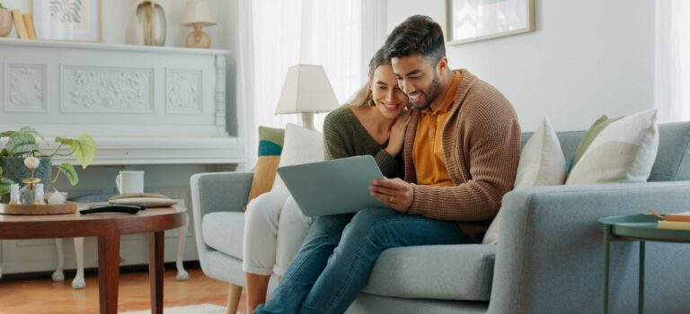 Couple sur un canapé en train de rechercher un bien immobilier sur un ordinateur portable