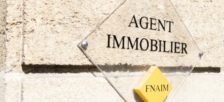 Inscription Agent immobilier et Logo FNAIM sur une plaque transparente posée sur un mur