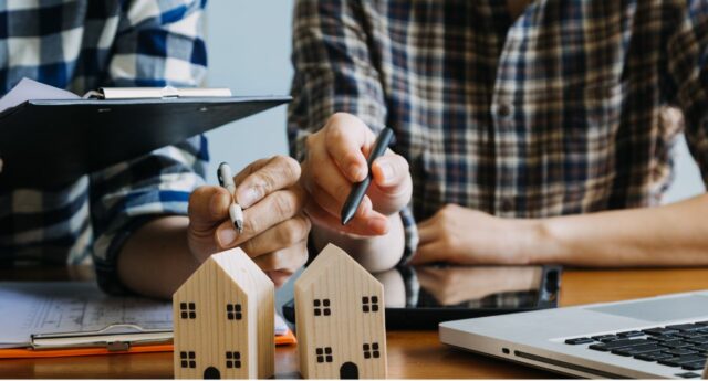 deux personnes en train de discuter d'un contrat devant deux maisons miniatures pour illustrer un partenariat autour du financement immobileir