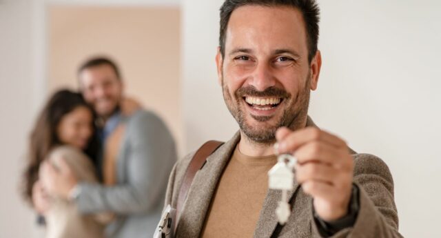 Agent immobilier souriant avec des cles dans la main et un couple enlace