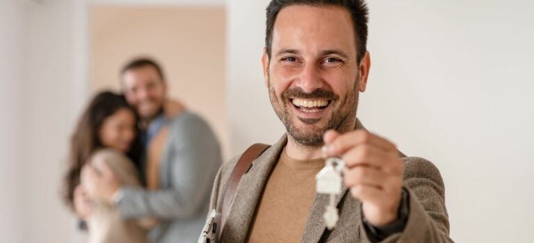 Agent immobilier souriant avec des cles dans la main et un couple enlace