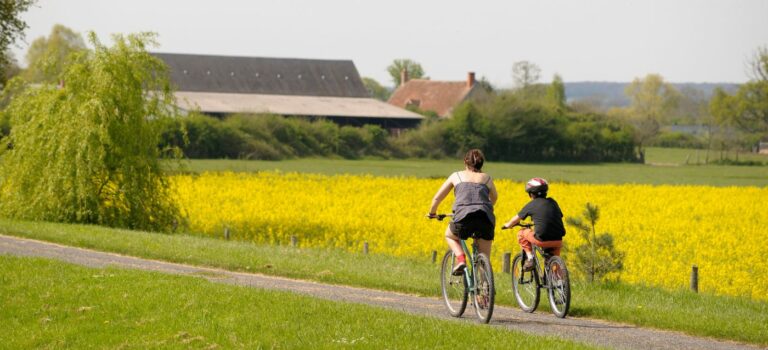 Une jeune femme et un jeune garcon en velo, sur une route de campagne avec maison arriere plan dans la Nievre