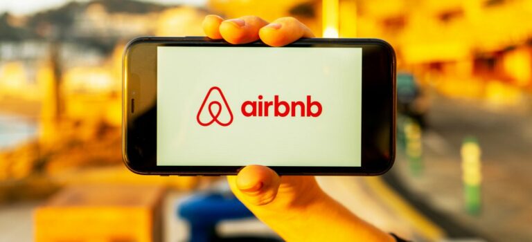 femme tenant dans sa main un smartphone avec logo Airbnb
