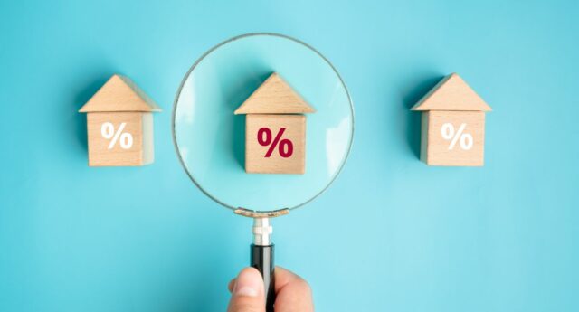 Main tenant une loupe scrutant des taux d'interets sur des maisons miniatures pour illustrer le credit immobilier