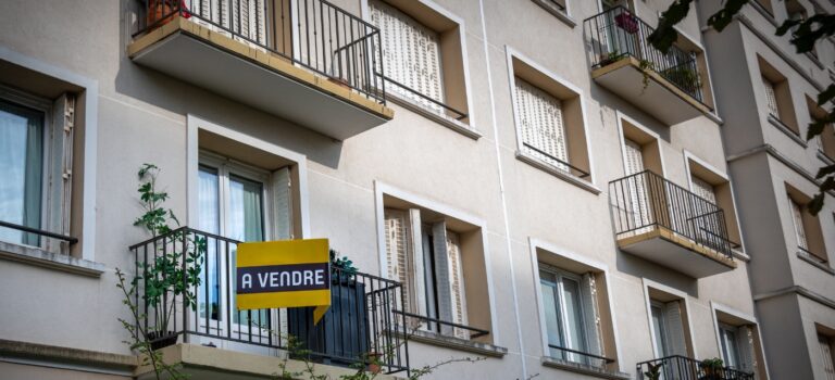 Immeuble avec pancarte A vendre accrochée à un balcon