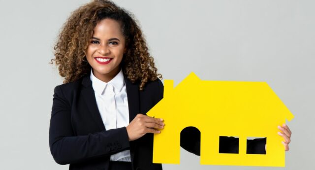 jeune femme souriante tenant un maison miniature entre ses mains