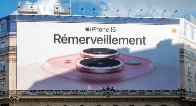 ffiche publicitaire géante Apple iPhone 15 couvrant les échafaudages des travaux de restauration sur la façade d'un immeuble parisien abritant un Apple Store