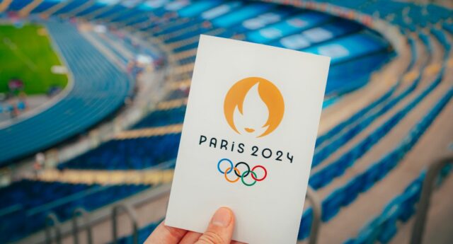 Mains tenant un carte avec le symbole Paris 2024 avec le stade de France en toile de fond