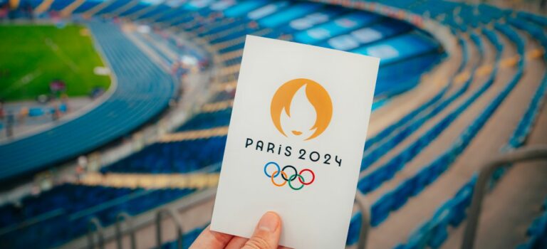 Mains tenant un carte avec le symbole Paris 2024 avec le stade de France en toile de fond
