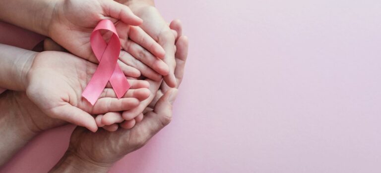 mains tenant un ruban octobre rose pour illustrer le cancer du sein