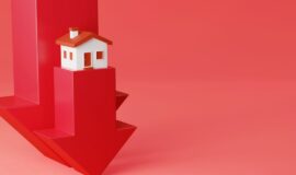Maison miniature posee sur une fleche rouge qui pointe vers le bas pour illustrer la baisse de l'immobilier