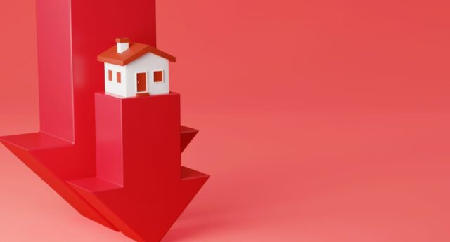 Maison miniature posee sur une fleche rouge qui pointe vers le bas pour illustrer la baisse de l'immobilier