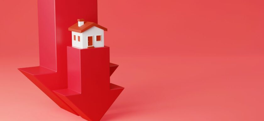 Maison miniature posee sur une fleche rouge qui pointe vers le bas pour illustrer la baisse de l'immobilier