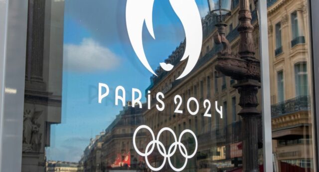 Reflet du Logo Paris 2024 sur une porte vitree a Paris avec des immeubles en toile de fond