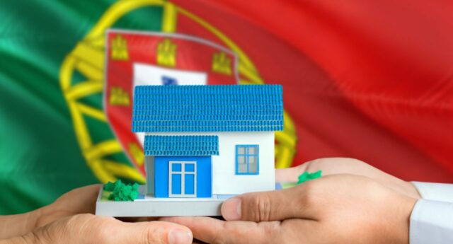 Couple tenant dans ses mains une maison miniature avec le drapeau portugais en toile de fond pour illustrer l'immobilier au Portugal