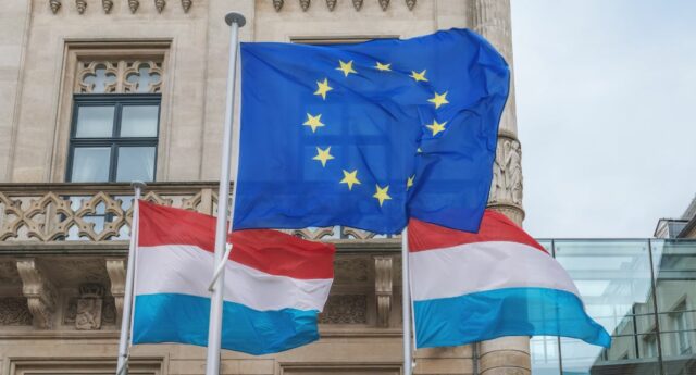 Drapeau de l'Union européenne flottant a cote de deux drapeaux du Luxembourg devant un batiment historique au Luxembourg
