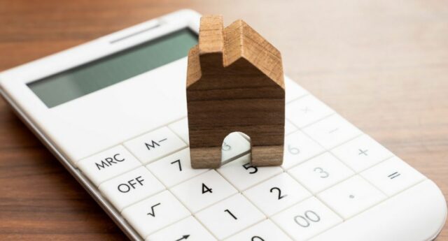 maison en bois miniature posee sur une calculette