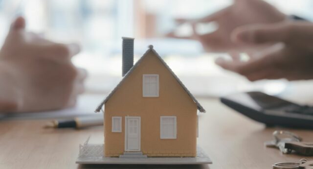 Maquette de maison sur une table, avec des mains en arriere plan pour illustrer conseil immobilier