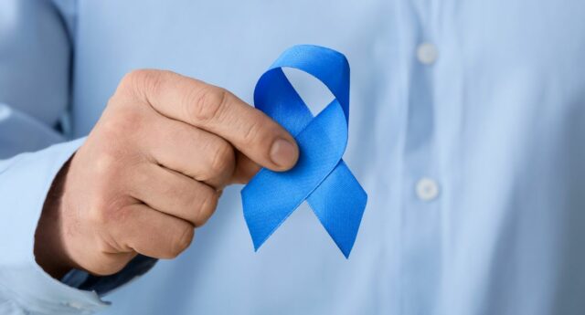 Main d’un homme tenant un ruban bleu, symbole de la sensibilisation au cancer de la prostate, sur fond de chemise bleue