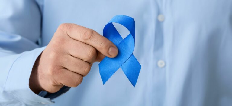 Main d’un homme tenant un ruban bleu, symbole de la sensibilisation au cancer de la prostate, sur fond de chemise bleue