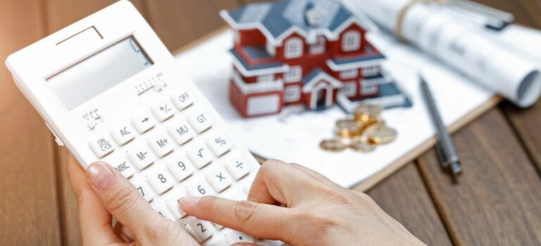 Main feminine calculatrice a la main avec maison miniature et dossiers en arriere plan
