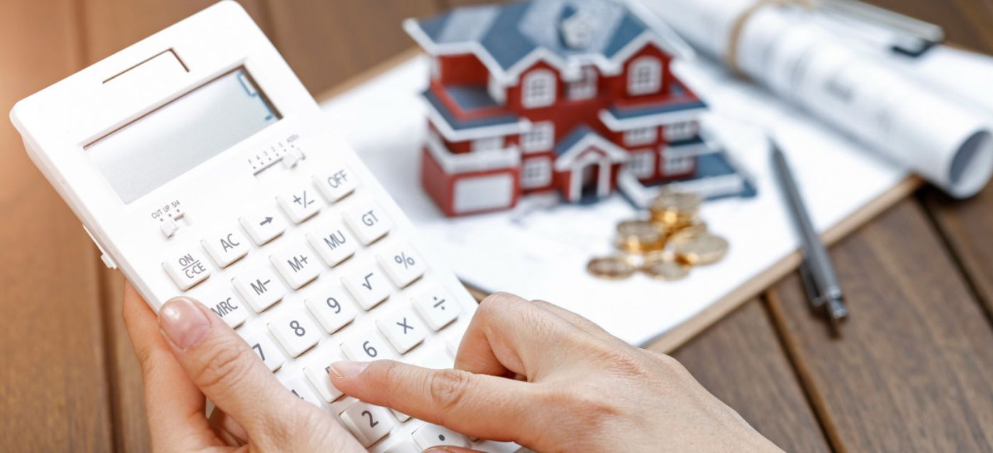 Main feminine calculatrice a la main avec maison miniature et dossiers en arriere plan