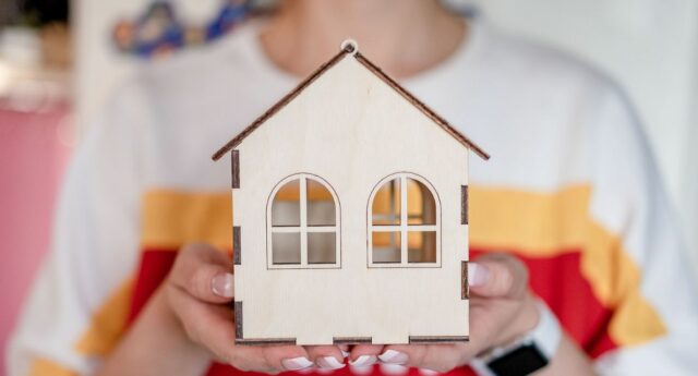 Personne tenant une petite maison en bois symbolisant un projet d'achat immobilie