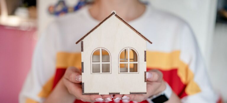 Personne tenant une petite maison en bois symbolisant un projet d'achat immobilie