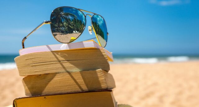 des lunettes de soleil posees sur une pile de livres sur une plage avec la mer au fond