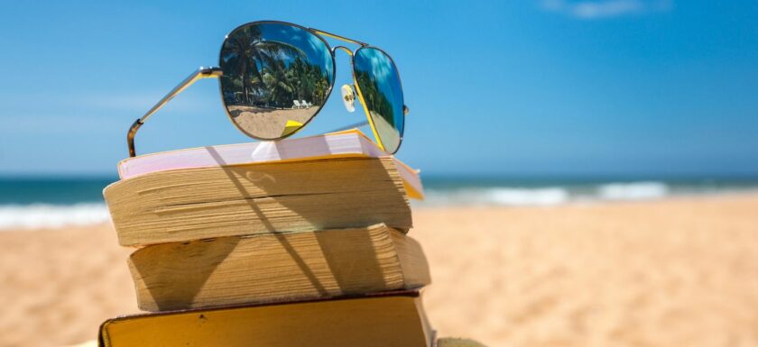 des lunettes de soleil posees sur une pile de livres sur une plage avec la mer au fond