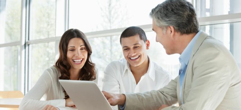 Conseiller professionnel montrant des informations sur un ordinateur portable a un jeune couple souriant lors d'une reunion dans un bureau lumineux